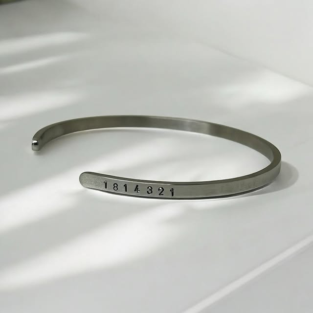 Bracelete fino de aço com código gravado, sobre mármore branco