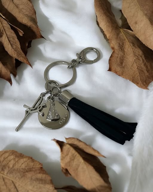 Chaveiro com medalha gravada, crucifixo e tassel preto sobre tecido branco